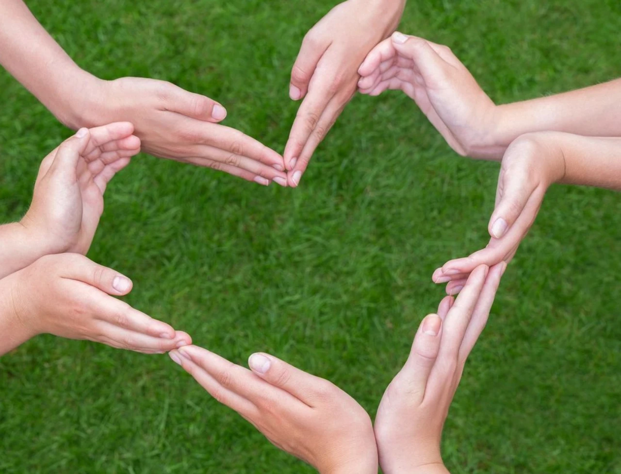 Hands forming a heart shape on green grass.